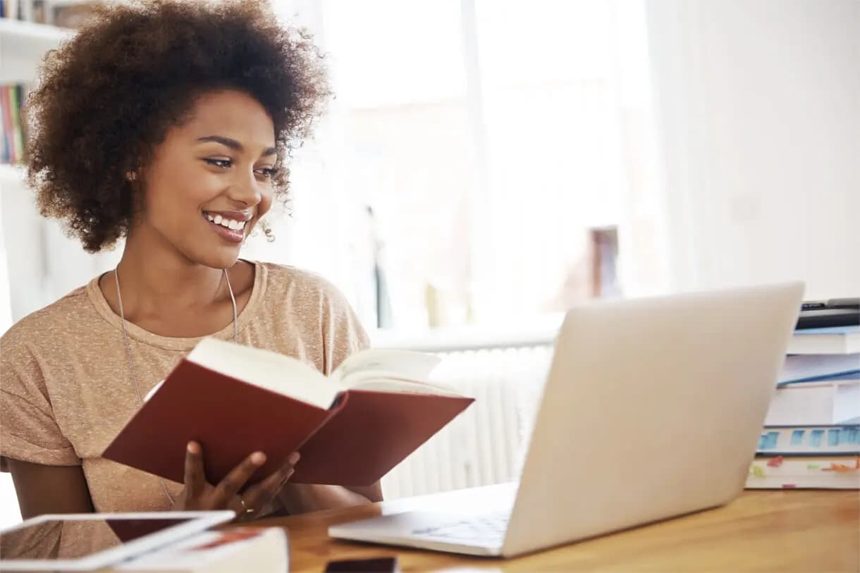Student studying at a desk with a book and laptop